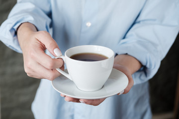 Woman holding cup of coffee. Female hands with cup of black tea on beige background. Close up