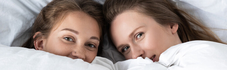 panoramic shot of two lesbians lying under white blanket in bedroom