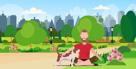 Fototapeta premium poor bearded man with dog sitting in urban park beggar guy begging for help homeless jobless concept cityscape landscape background full length flat horizontal