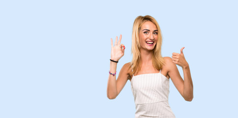 Fototapeta na wymiar Young blonde woman showing ok sign and thumb up gesture over isolated blue background