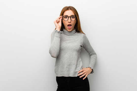 Redhead girl over white wall with glasses and surprised