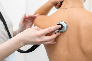 Woman doctor therapist listening with a stethoscope to a back, young female patient