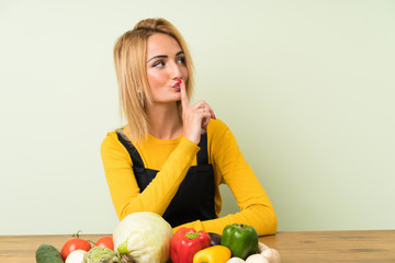Young blonde woman with lots of vegetables doing silence gesture