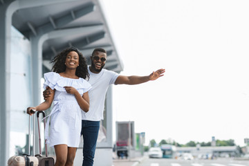 Young african couple standing near airport trying to stop car