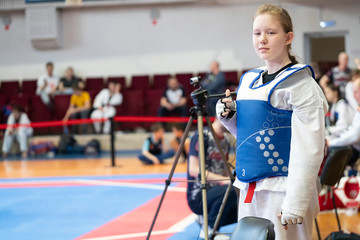 a girl participating in Taekwondo competitions in a blue protective vest on the background of Taekwondo competitions close-up