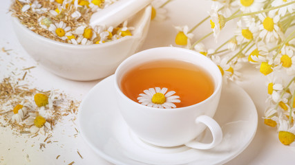 Rural still-life - cup of brewed chamomile tea on the background of a bouquet of daisies, closeup