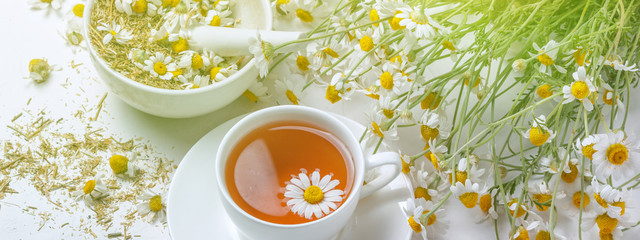 Rural still-life - cup of brewed chamomile tea on the background of a bouquet of daisies, closeup