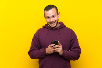 Fototapeta premium Colombian man with sweatshirt over yellow wall sending a message with the mobile