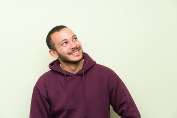 Colombian man with sweatshirt over green wall laughing and looking up