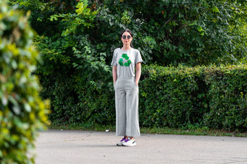 Young smiling attractive woman in gray t-shirt with recycle symbol in park.