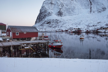 Naklejka premium Fishing boat anchored on pier with red village in winter at Lofoten