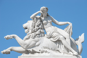 Old statue of sensual renaissance era woman laying on big lion at blue smooth background, Potsdam,...