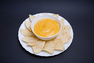 Queso chedar vegano con nachos para mojar sobre fondo negro.