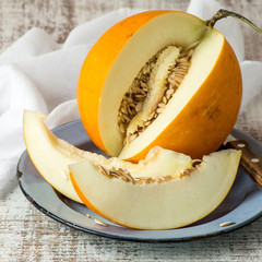 Ripe yellow melon, cut into pieces, on a round blue plate on an old table. Selective focus.