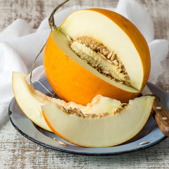 Ripe yellow melon, cut into pieces, on a round blue plate on an old table. Selective focus.
