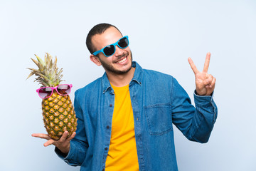 Colombian man holding a pineapple with sunglasses smiling and showing victory sign