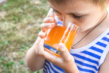 A little boy drinks juice with ice in nature.