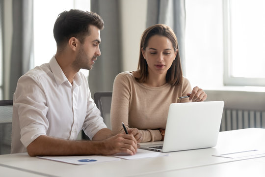 Female mentor talking teaching male colleague intern looking at laptop