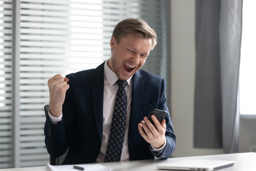 Euphoric happy businessman wear suit celebrate mobile win