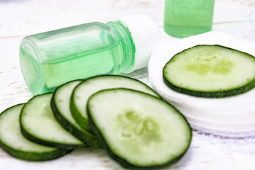 Sliced cucumber and a bottle of cucumber extract on a white wooden table and a white background. Liquid cosmetics for skin care.