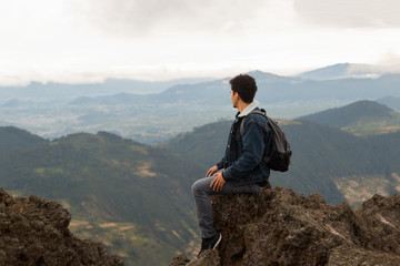 Naklejka premium Latin man sitting on top of a cliff with the mountains behind him