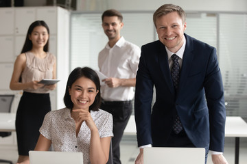 Smiling diverse business leaders posing with computers and team people