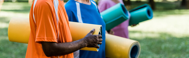 panoramic shot of senior and multicultural pensioners holding fitness mats