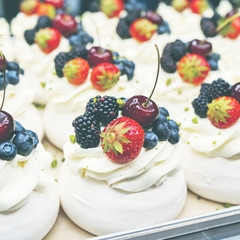 Pavlov cakes with fresh berries and cream. Lie in rows on a baking sheet in the confectionery shop.