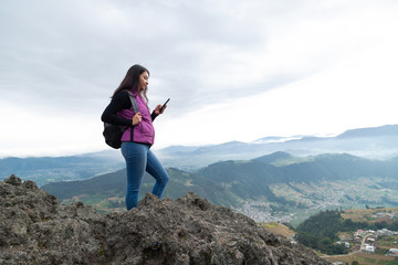 traveling woman on top of the mountain at dawn with the sky clouding sending a message with her cell phone- Hispanic traveler