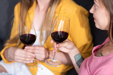 partial view of two lesbians holding wine glasses in living room