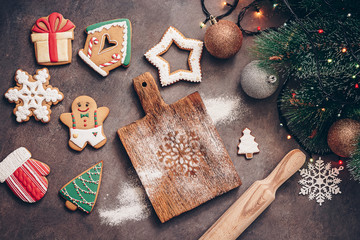 Christmas baking background. A variety of ginger glazed gingerbread, a pine branch and a garland on a dark rustic background. Top view, flat lay.