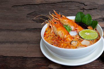 Tom Yum Goong or Shrimp soup spicy sour Soup Traditional food in Thailand contains chili lime lemongrass lime leaf, along with cooked rice in a white dish on the old wood background from top view.