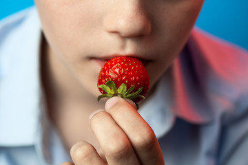 a boy biting red strawberries on a blue background