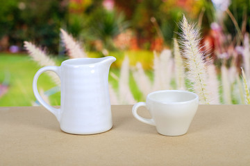 White coffee cup and jar on wood table with nature background.