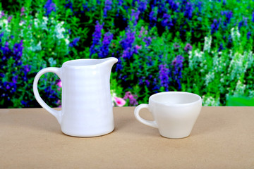 White coffee cup and jar on wood table with nature background.