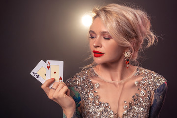Blonde woman with a beautiful hairstyle and perfect make-up is posing with playing cards in her hands. Casino, poker.