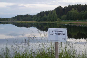 the sign "bathing is forbidden" in Russian installed on the shore of a forest lake