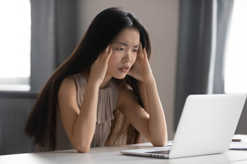 Stressed asian businesswoman feel headache at work looking at laptop