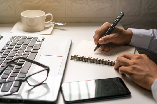Businessman is taking a note on the notebook  from the financial imformation from laptop computer .business work concept.