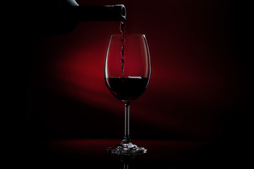 Obraz na płótnie Canvas Red wine being poured in a wine glass on a dark red gradient background. Studio close-up shot.