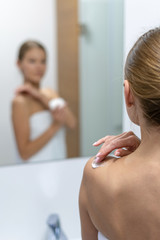 Woman applying body cream on shoulder in bathroom