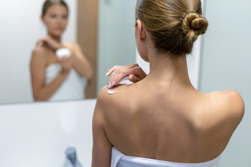 Woman applying body cream on shoulder in bathroom
