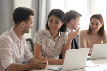 Happy diverse employees talking laughing working together with coworkers laptops