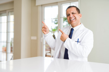 Middle age doctor man wearing medical coat at the clinic smiling and looking at the camera pointing with two hands and fingers to the side.