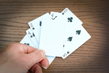 white blank mock-up card in dealer's hand, playing cards and wooden table background