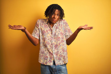 Afro man with dreadlocks on vacation wearing floral shirt over isolated yellow background clueless...
