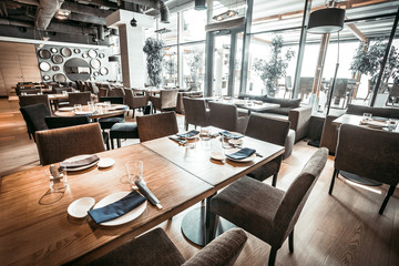 Spectaculair interieur van het eigentijdse restaurant in stijlvolle grijstinten. De grote zaal met de houten tafels, stoelen en fluwelen banken. Glazen wand met toegang tot het terras.
