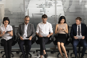 Diverse applicants sit on chairs in row in waiting room