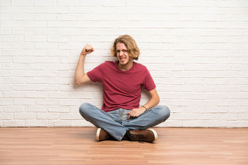 Blonde man sitting on the floor doing strong gesture