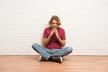Blonde man sitting on the floor scheming something